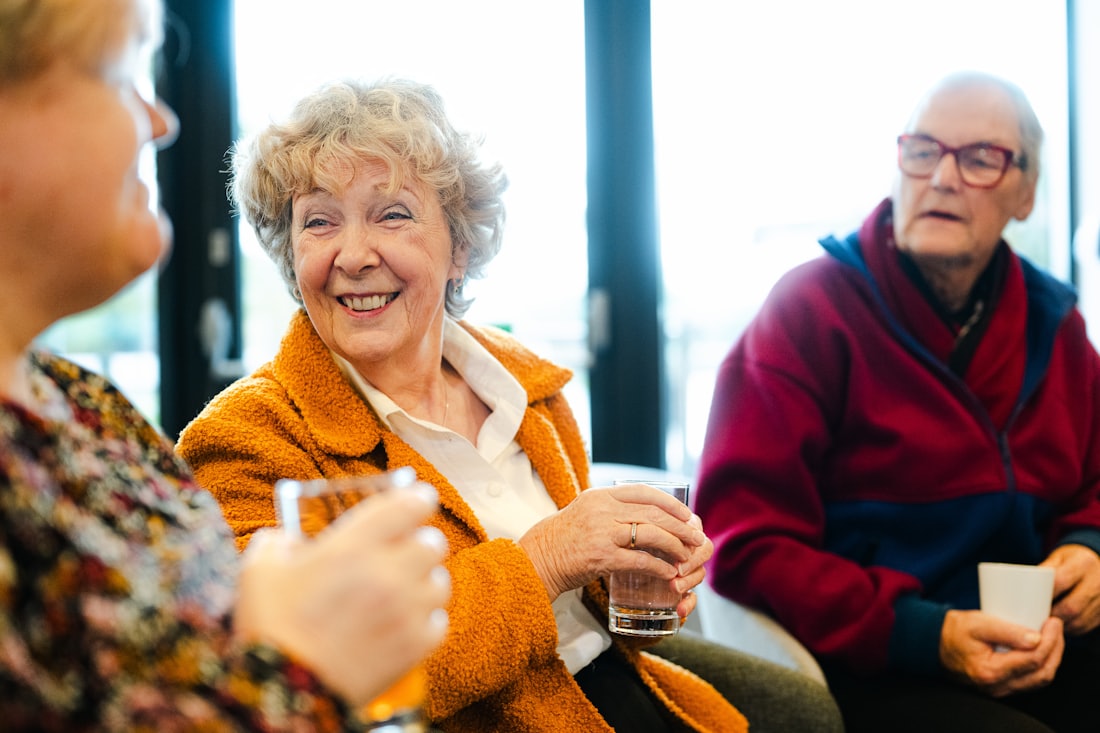 Three friends in their seventies laughing together over a cup of tea