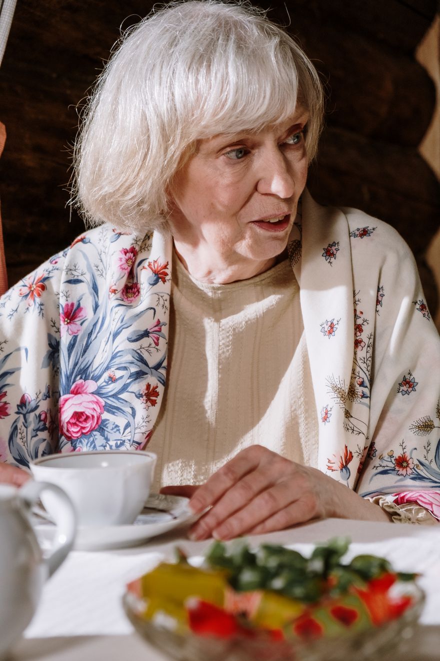 A woman in her late seventies with a cup of tea, mid-conversation at home
